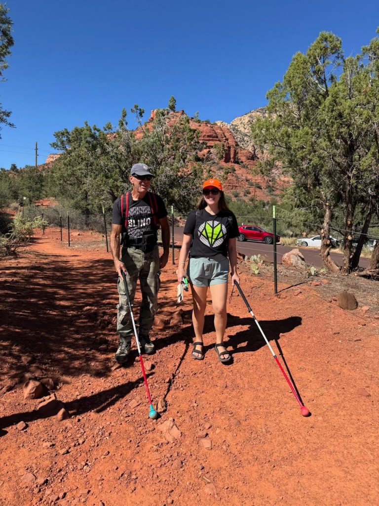 A photo of Dave and Monica walking on a trail using their all-terrain canes. 
